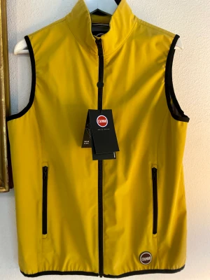 Colmar Softshell Vest stl M (50) - Helt oanvänd ny Colmar gul väst i stl M (50) med alla etiketter kvar. En klassisk och bekväm väst i minimalistisk design tillverkad i Softshell av polyesterblandning med vind- och vattenavvisande material. 