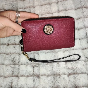 Plånbok - En superfin, vinröd, rymlig plånbok med guldiga och svarta detaljer. Säljer för så bra pris eftersom den inte används. 16 x 10 cm. 