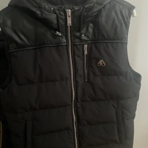 Moose Knuckles väst herr - Jag använder inte den längre den är i ganska nyskick förutom det som syns på tredje bilden där det är ett hål som vi sytt igen som inte syns eftersom den är under luvan. Det är  5 fickor på västen 3 på utsidan och 2 på innsidan. Pris går att diskutera.