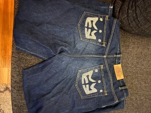 Y2K Jeans - Väldigt snygga Y2K Jeans som har unikt tryck på båda bakfickorna, inga skador förutom ytterst lite slitna längst nere på byxorna. Storleken är 36 och är breda.
