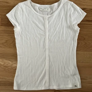 Ribbad vit t-shirt - En jättegullig topp med fina detaljer som tyvärr inte kommer till användning längre. Den är i storlek 15/16 och passar xs/s, materialet är stretchigt så jag skulle säga att den passar större också. Kontakta mig för mer information 💓