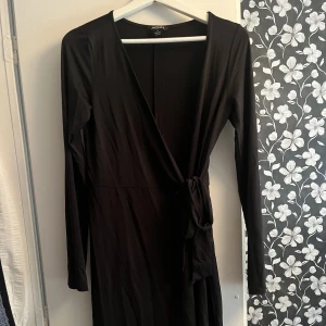 Svart sidenklänning - Svart sidenklänning från MONKI som knytes omlott. Väldigt stretchigt material så passar olika storlekar beroende på hur man vill att den ska sitta. På mig som är 170cm går den till knäna.  Storlek S.