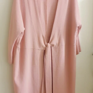Ljusrosa cardigan - Ljusrosa cardigan från Pieces. Lätt och somrig tyg. Knälång med snöre/ bälte fram (se bilder). Ärnarna är 3/4.   