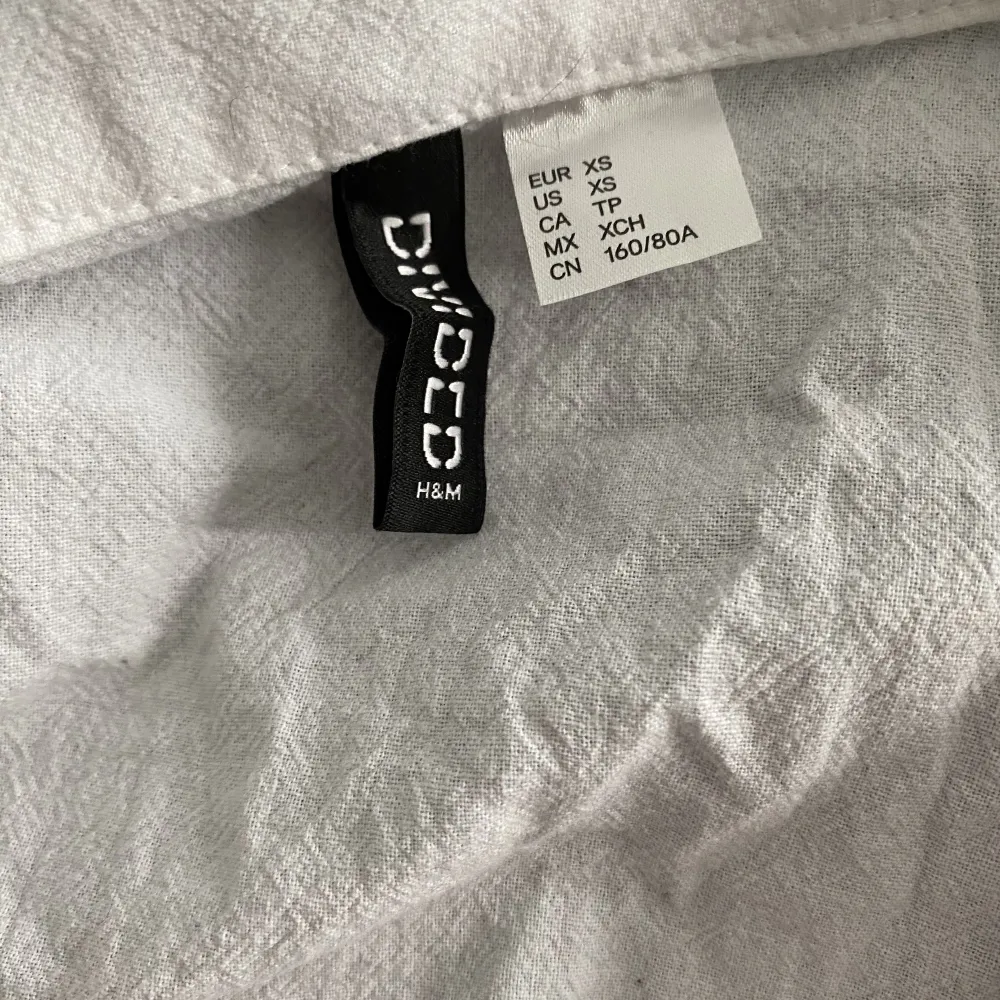En vit cropped topp i skjort tyg från Devided H&M i storlek XS. Använd en gång med en liten fläck på snörningen, syns inte mycket. Stryks innan köp. Köpet är bindande . Toppar.