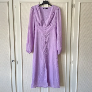 Gina Tricot midiklänning  - Superfin lila klänning från Gina Tricot som tyvärr inte passade mig. Ingen lapp kvar men aldrig använd. Finns dock ett märke vid några knappar men det borde gå bort i tvätten. Djup v-ringning, knappar hela vägen i fram och smock i ryggen. Nypris 499kr!