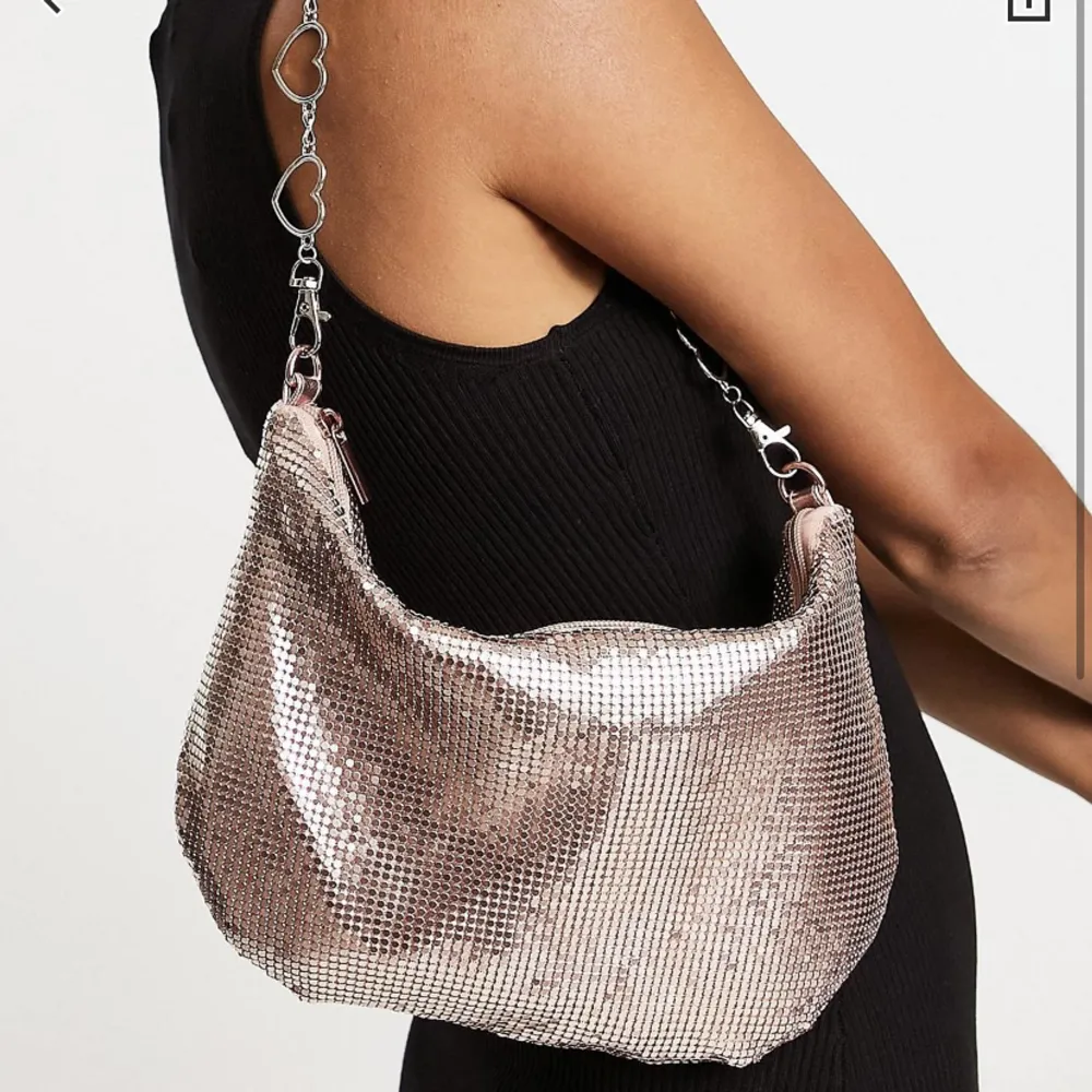 Roseguld/rosa handväska med metallhjärtan som band. Helt oanvänd, har prislapp fortfarande.  Orginalpris: 429kr. Accessoarer.