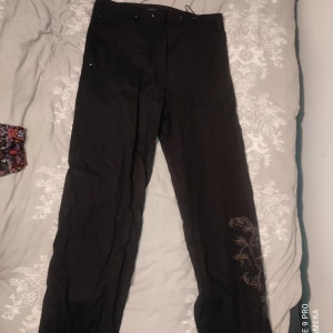 Ballon aktiga byxor - Byxor i ungefär samma tyg som balloon byxor. Svarta med coolt broderat motiv på ena benet. Justerbara snören både i midjan och vid fötterna. Storlek 36 men kan passa 38. Pris kan diskuteras