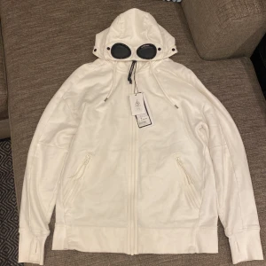 CP Company Google Hood Zip - Tjena säljer min vita cp company zip hoodie som jag köpte på NK i Göteborg. Skicket är typ 9/10, utsidan är super fin men lite missfärgning från smink på insidan av en tjej… annars inga problem över huvudtaget. Kan skicka fler bilder i DM. Nypris 2499kr