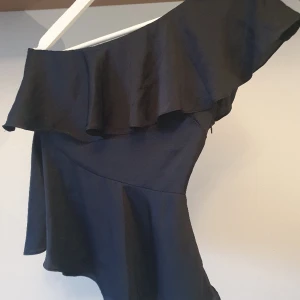 One shoulder topp med volang  - One shoulder mörkblå topp med volang. Dold dragkedja i sidan! Storlek 36. Perfekt till nyår! 