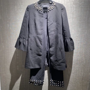 Kavaj och kostymbyxor - Ett jättefint set med  kavaj samt kostymbyxor. De har jättevackra pärlor broderade på. Ett spänne på kavajen har gått sönder (ringade in i rött), så det går bara att knäppa en av knapparna. Kavaj: S, Kostymbyxor: XS Skriv priv för mer bilder och info.