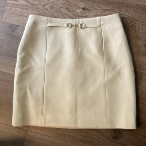 Beige kjol från H&M - Kort beige kjol med gulddetals fram från H&M!🎀Har använd ett par gånger endast och har jättebra skick💕