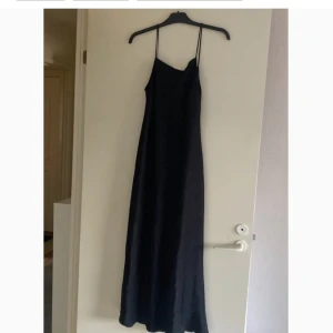 Satin slät klänning i svart  - Mycket bra skick, en vadlång klänning i följsam satin av viskos. Från zara, Klänningen har smala axelband. Klänningen framhäver kurvor då den är lite smalare i midjan och mer vid mot fötterna. Jag är 170 cm och den är till vaderna på mig.