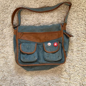 Axelremsväska - Demin axelremsväska köpt här på plick som jag inte använder längre. Den har många fack på insidan (se bild 3). Pins tillkommer, dem går att ta av!💕 skriv för fler bilder eller eventuella frågor! Tveka inte på att fråga om priset också!❤️