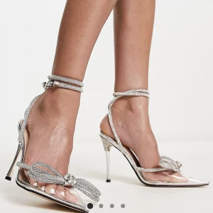 Klackskor med rosett i strass  - Silverfärgade. Klackhöjd: 10,5. Storlek 39. Endast använda en kort stund på en kväll på ett bröllop, därför är dem så gott som nya och super fina verkligen.  Kan hämtas i Malmö, eller fraktas. 