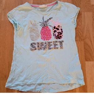 T-shirt  - T-shirt med tryck i storlek 146/152, skulle säga att den passar XS. I bra skick, har bara tappat vissa av diamanterna på ananasen i mitten (inget som märks av). Kan fraktas, köparen står för frakten💕