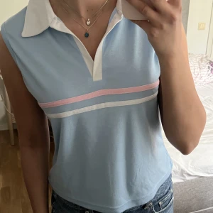 Blå topp - Super söt blå piké liknande topp med vit krage och rosa-vita ränder över bröstet. Inga defekter! Står XL på lappen men sitter mer som en S-M🫶💕