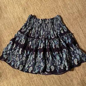 Söt kjol med resår i midjan som gör att den passar många storlekar. Använd av tjej i 8-årsåldern. Fin blå färg med paisleymönster. Saknar storleksmärkning.