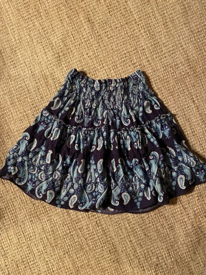 Kjol med resår - Söt kjol med resår i midjan som gör att den passar många storlekar. Använd av tjej i 8-årsåldern. Fin blå färg med paisleymönster. Saknar storleksmärkning.