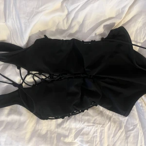 Snörad svart baddräkt  - Svart baddräkt med snörning fram sidor och bak. Går att välja hur mycket som ska synas eller ej  Stl s, mycket stretchig. Passar även som top till jeans 