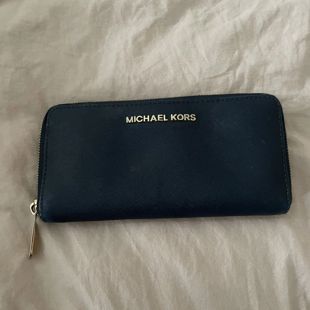 Snygg plånbok från Michael Kors, mörkblå med guld detaljer. Den har tappat guld på lite ställen men inget som märks jätte mycket. Ny pris är 1200kr. . Övrigt.