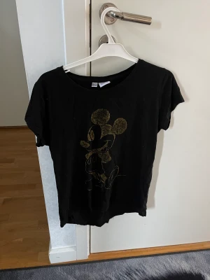 T-shirt  - En väl använd svart Disneytröja. Med en guldig Musse på. Lite sliten men inte mycket. Perfekt för en sommardag då den är väldigt sval. 