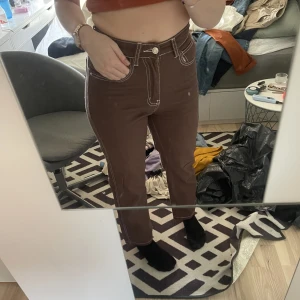 Bruna byxor med vit söm - Skitcoola bruna tygbyxor med vit söm som man matchar snyggt med en vit tröja eller skjorta. De är högmidjade och rätt tighta upptill men är vida nedtill. Köpa från SHEIN men väldigt fint skick. 