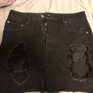 Svart jeanskjol  - En svart jenas kjol med större slitningar på ena sidan och öppet på den andra sidan. Kjolen är från bikbok och använd ett par gånger