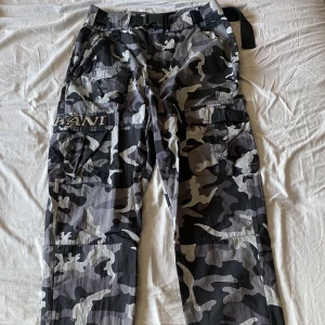 Karl Kani Cargo - Byxorna är i Nylon med inbyggt justerbart bälte och klassiska cargo fickor med zippers. Använt men ändå gott skick, kunde inte hitta något hål!
