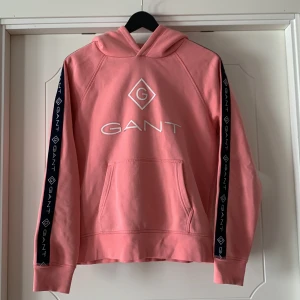 Rosa hoodie Gant  - Jättefin rosa hoddie från Gant. Storlek 170 men tycker den är liten i storleken så kan passa 160cm. Använd väldigt få gånger. Trycket har tyvärr släppt (se bild 3) men går enkelt att fixa med textillim.