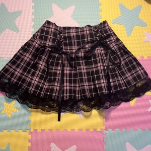 Svart lila rosa kjol snygg - Säljer för att den inte är min stil, super snygg och söt. Banden som sitter runt den kan spännas och dras ut så de passar en i midjan. Kjolen har även en dra kedja. Fläckfri & ej söner. Mått i midjan utspänd: 80cm, spänt midjemått: 60cm längd: 35cm. 