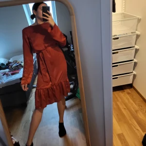 Sidenklänning med knytband - Väldigt elegant, brons-vin-röd klänning i sidenaktigt material, volang nere och knytband i midjan. Aldrig använd. Storlek S. Hämtas i malmö/gbg eller skickas mot fraktkostnad. 