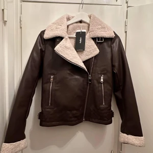 Jacka - Helt ny skinnjacka i mörkbrunt med mudd. Stl XS. Jätte fin och åtsittande. Bilden ger ej rättvisa på färgen, skriv för fler bilder 