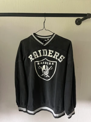 Svart tröja med märke på  - En svart tröja med trycket ”Raiders” på. Vilket jag tror är ett lag i amerikansk fotboll 🏈. Den är köpt på hm. Storlek xs. Och den är i väldigt fint skick! 🤩
