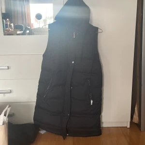 Lång väst - Lång svart väst med luva. Den är oanvänd har bara provat den på. Den är i xs men passar m också. Skriv vid intresse eller bild❤️