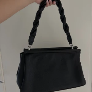 Svart väska - En svart rymlig väska från NA-KD. Perfekt till vardags! Går att ha i två ”lägen”, en där den ser mer stängd ut (som på bilderna) och en där väskan ser mer ”öppen” ut. 