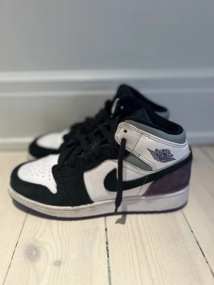 NIKE Jordan 1 Mid SE ”Varsity Purple” - Säljer ett par NIKE Jordan 1 Mid SE ”Varsity Purple”. Storlek EU 36,5 / UK 4 Färg svart och lila mocka, vitt läder  Fint skick, sparsamt använda, se bilder ( finns fler att få) En liten 4 mm gul fläck på sidan se bild, därav priset. 