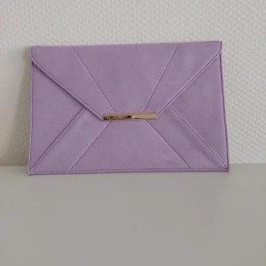 Lila kuverväska - En lila kuverväska med guld detalj. Den är oanvänd och i nytt skick. 