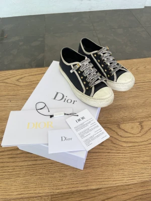 Dior skor - Säljer mina WALK'N'DIOR SNEAKER black cotton canvas då det inte kommer till användning. Nypris 9000 kr. Kvitto samt box och dustbag finns kvar. Det har ett litet hål i ena sulan dock ingenting som påverkar användningen av skorna. Motsvarande 37 i storlek.
