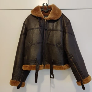 Pilotbomber jacka i äkta lammskinn! - Pilot bomberjacka från British Royal Airforce. Jackan är gjord av lammskinn och är helt fodrad med lammull.   Storlek XL. Passform: Classic Färg: Mörkbrun Skick: Helt ny   Köpte för 6500kr, säljer för 5000kr.   Finns i Stockholm!