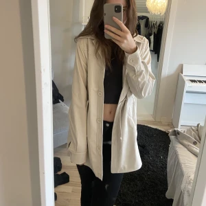 Regnkappa - Beige regnkappa ifrån nakd. Kan justeras med banden i midjan. Storlek 36. Normal passform. Använt en gång. 