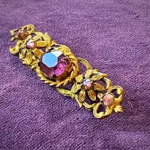 En vintage guldfärgad brosch med lila stenar 