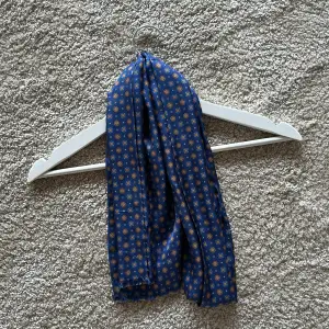 Silkesscarf från John Henric i en snyggt mönster med blå som basfärg! 100% Silke och använd en gång, dvs i nyskick!