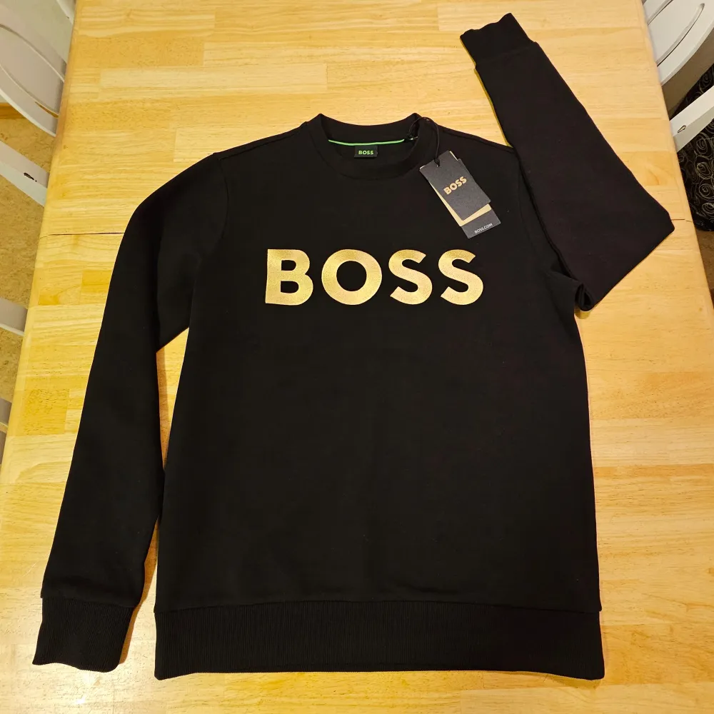 Helt ny Hugo Boss tröja i strl XS.  Super snygg svart tröja med texten som är i guld broderat på bröstet. Etiketten kvar, endast provad en gång men sedan dess legat i garderoben. Och tyvärr kan jag inte returnera för att de gått för lång tid.. Tröjor & Koftor.