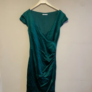 Festklänning  - Festklänning i polyester. Mörk grön. Slutar ovanför knät. 