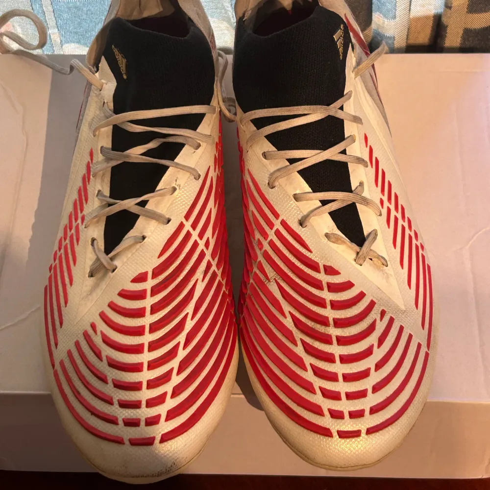 Till salu: Adidas Predator Edge i vitt och rött. Dessa skor är designade för ultimat prestanda på fotbollsplanen med en perfekt kombination av komfort, grepp och bollkontroll. Perfekt för spelare som vill ha överlägsen känsla och precision. . Skor.