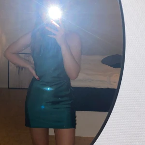 Grön Satinklänning - Halterneck klänning i grönt satinmaterial. Använd fåtal gånger så är i nyskick. Ger en väldigt fin siluett. Öppen rygg. Passar strl XS-S