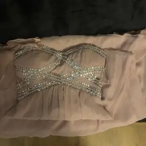 En balklänning utan band, den är ljus rosa med strass. Vet inte längden men vid önska kan jag ta mått på den, finns även bilder på om man vill se