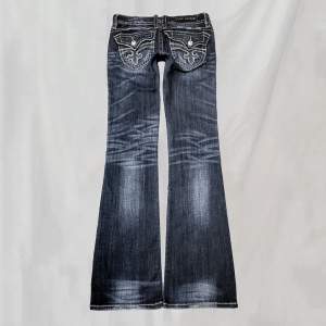 Midja:73 innerben:84 Lågmidjade jeans från Rock Revival. Strl w26. Nötningar enligt bild men är även del av design. Ögglan till knappen gått upp lite, går fortfarande att använda men bör vara försiktig/sy. Lite nötta fotändar men överlag bra skick🤍