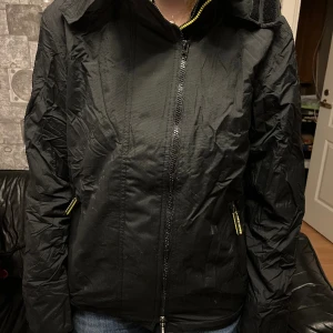 Superdry  - Svart jacka med gult fleecefoder Två dragkedjor fram, den ena saknar ”dragflärpen”  Storlek M  Prisförslag  Frakt tillkommer 