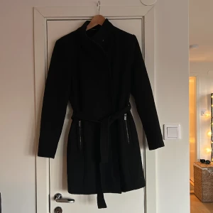 Kappa från vero moda - Svart kappa från vero moda med band i midjan och hög hals. Längden är ner till mitten på låret, och jag är 171 cm lång. ☺️ 